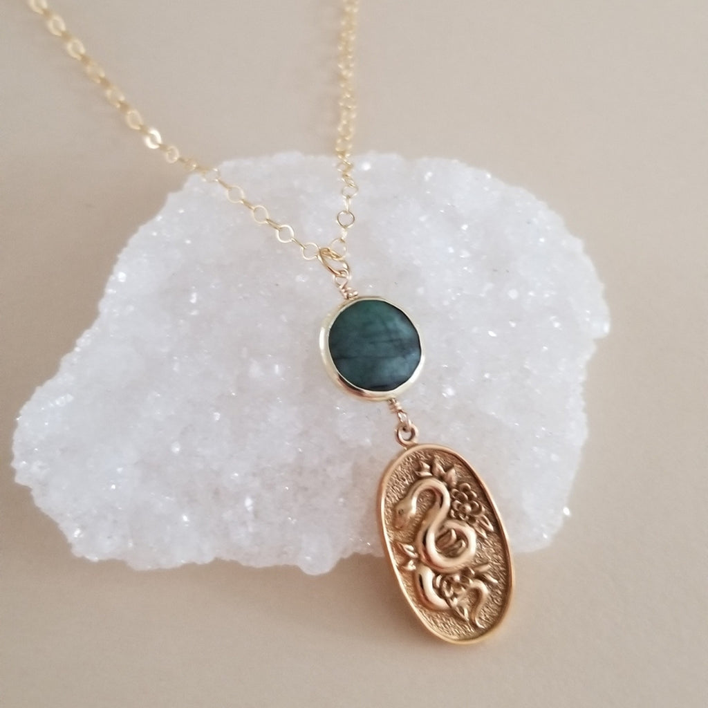 Gold snake pendant necklace with emerald gemstone, symbolizing transformation and elegance, perfect for statement jewelry lovers.