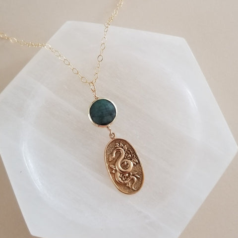 Gold snake pendant necklace with emerald gemstone, symbolizing transformation and elegance, perfect for statement jewelry lovers.