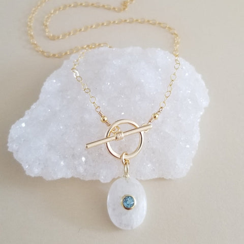 Handmade gold chain necklace with front toggle clasp, featuring a shimmering moonstone pendant and faceted blue topaz drop, elegant gemstone jewelry for everyday wear or special occasions.
