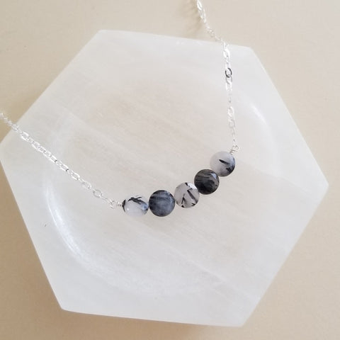 Handmade elegant necklace featuring a row of black rutilated quartz gemstones on a delicate chain, modern crystal jewelry with natural needle-like patterns.