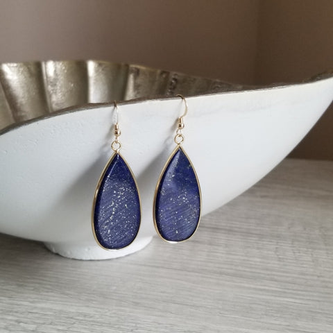 Teardrop-shaped blue earrings with gold accents on a white dish.