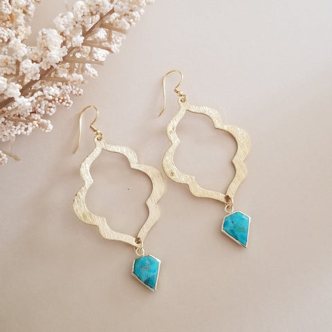 Gold earrings with turquoise drops on a beige background