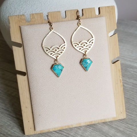 Gold earrings with turquoise stones on a wooden stand.