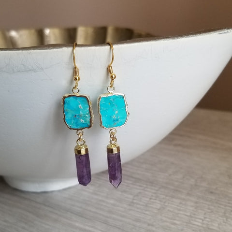 Turquoise and purple gemstone earrings with gold accents on a white dish.